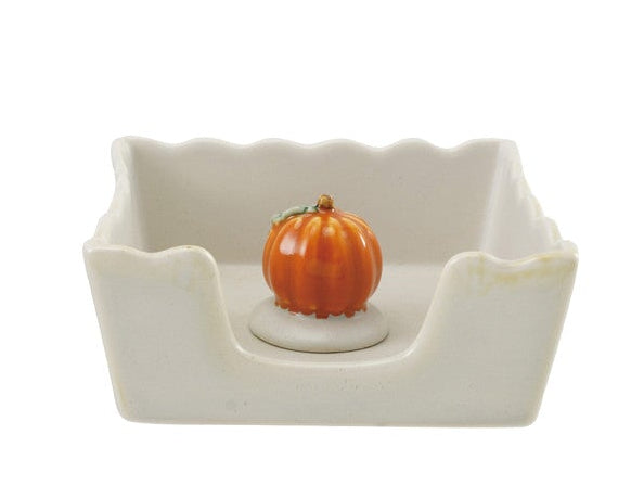 Stoneware napkin holder with scalloped edges with a small orange pumpkin weight.
